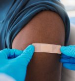 Closeup of young, healthy males arm with bandage after covid vaccine shot from medical doctor. Male patient wearing first aid plaster after medicine injection treatment from healthcare professional