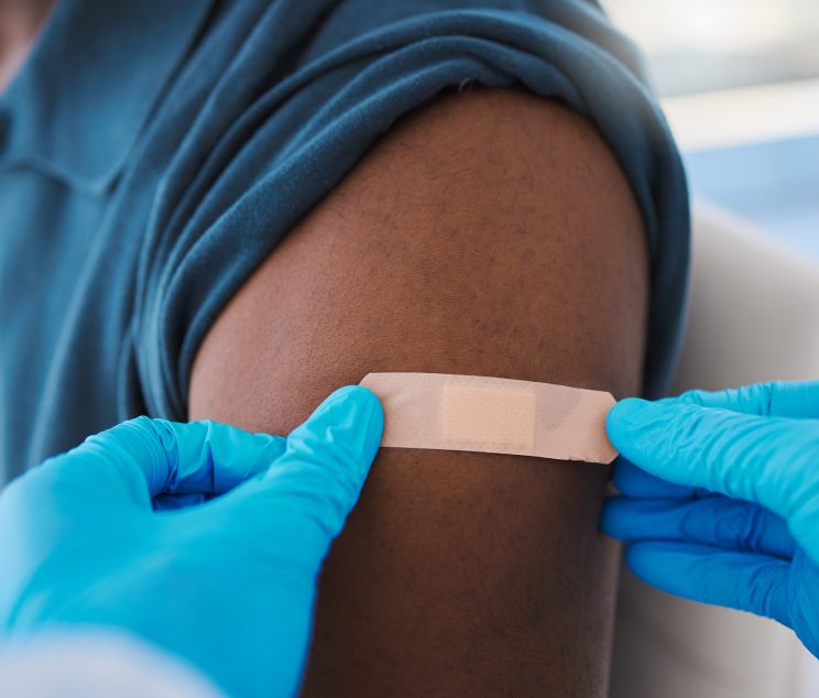 Closeup of young, healthy males arm with bandage after covid vaccine shot from medical doctor. Male patient wearing first aid plaster after medicine injection treatment from healthcare professional